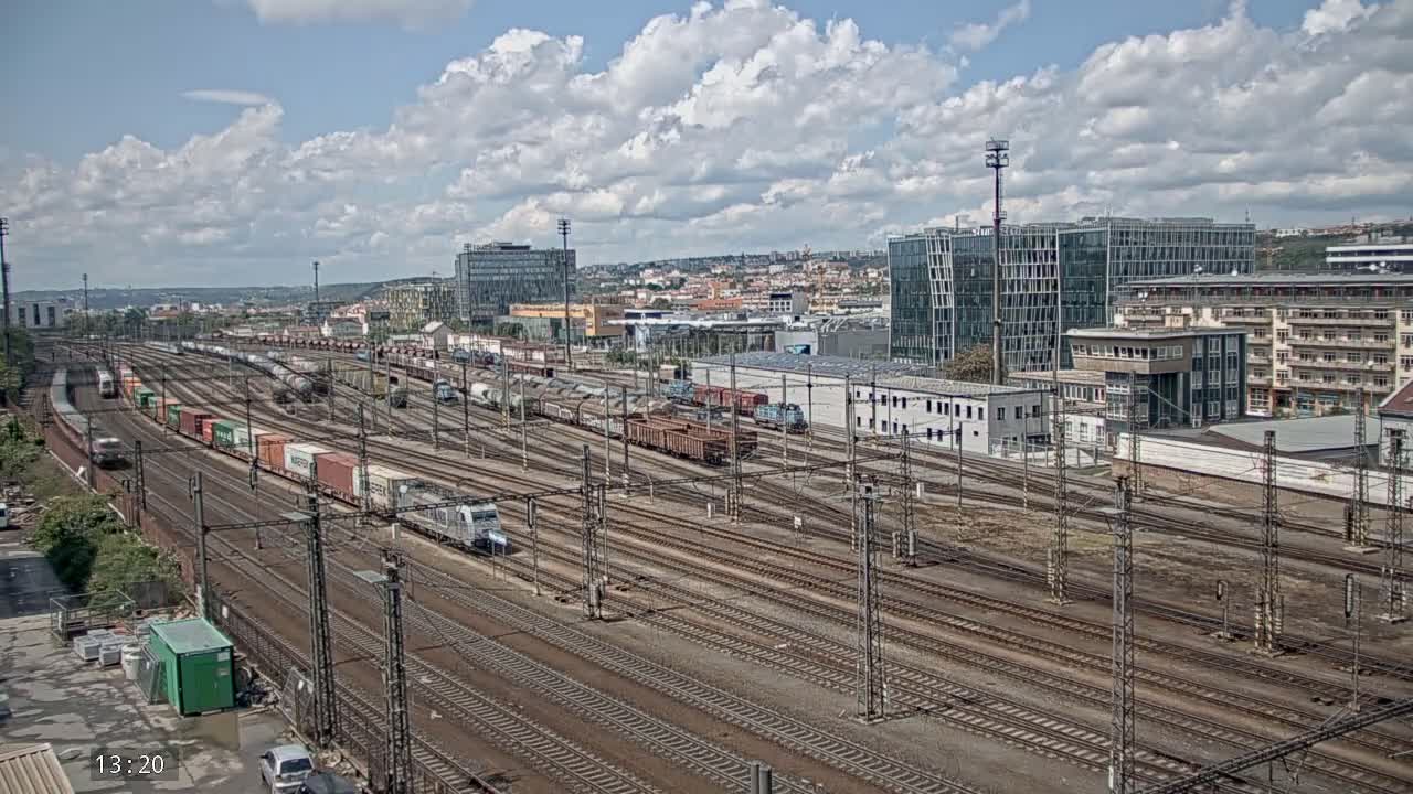 A large railway yard with numerous freight trains and tracks is visible under a partly cloudy sky.