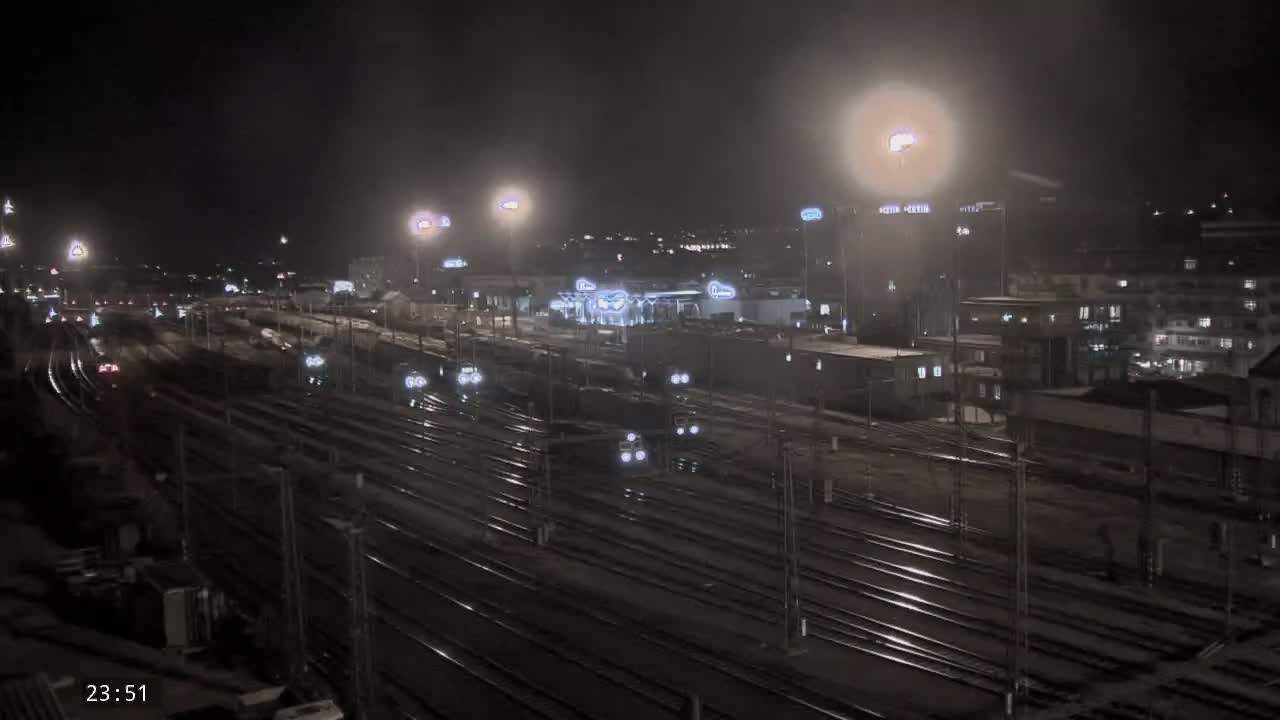 A nighttime, overhead view of a train yard with multiple train cars and tracks, illuminated by artificial lights.