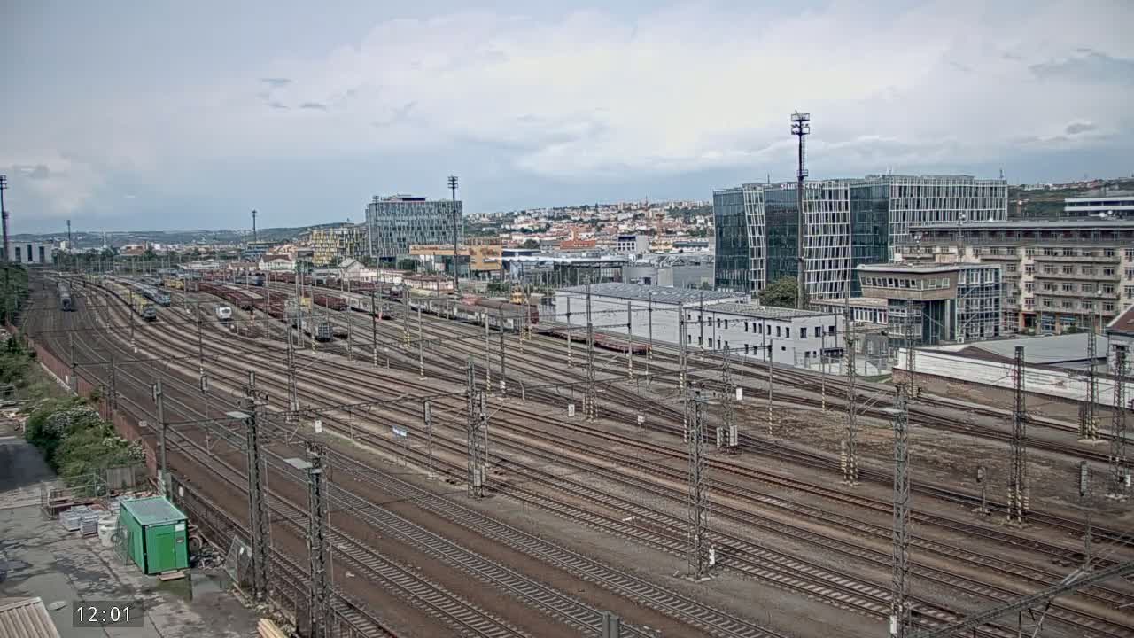 An expansive railway yard with numerous train cars and tracks, under a cloudy sky, is situated near a city skyline.