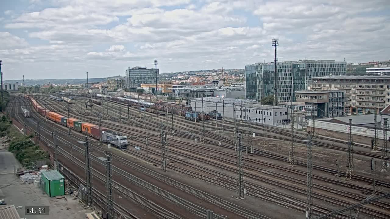 Numerous freight and passenger trains are situated on a sprawling network of train tracks in a city under a cloudy sky.
