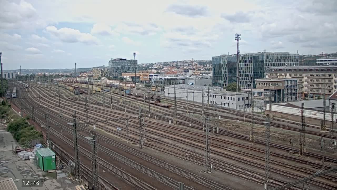 A sprawling railway yard with numerous tracks extends towards a city skyline under a partly cloudy sky.