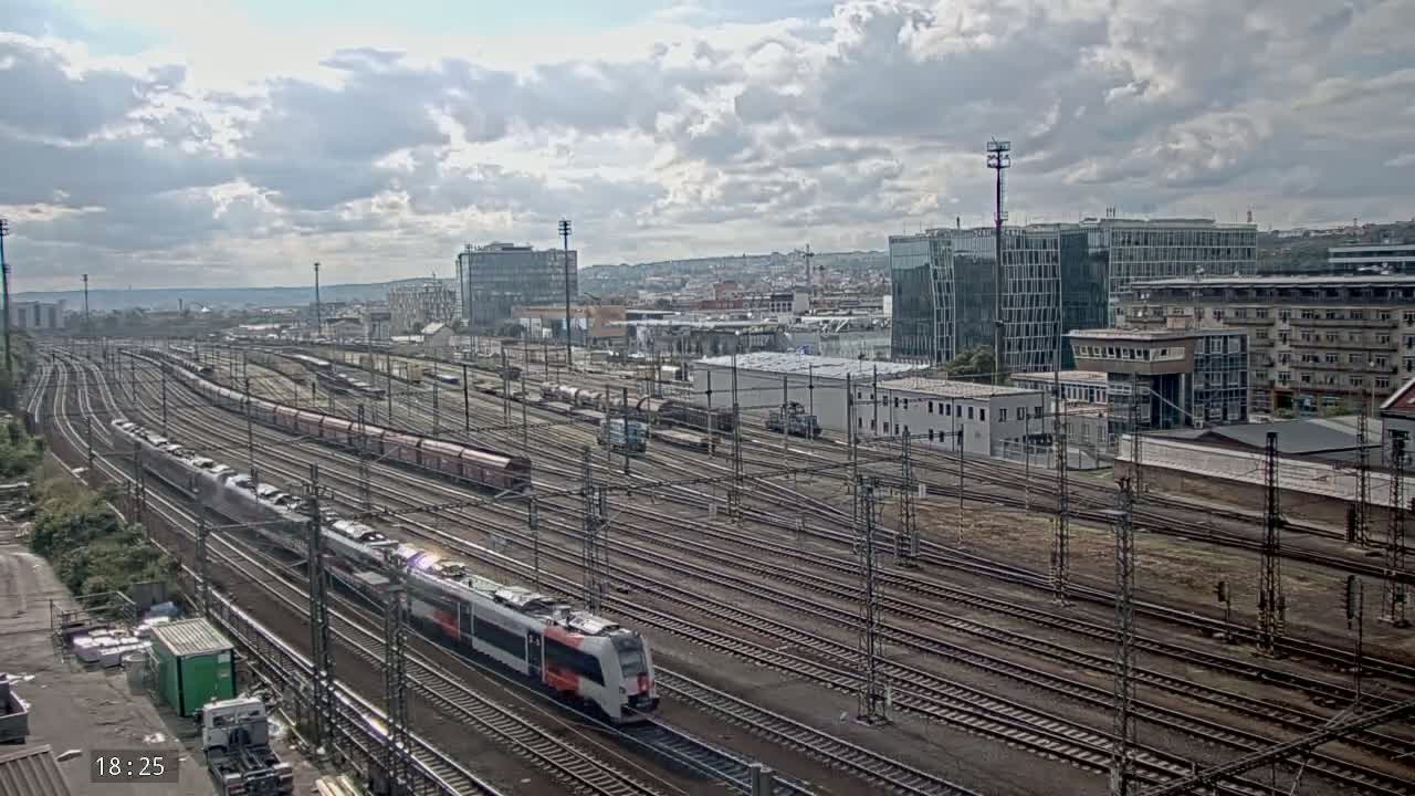 A high-angle, long shot of a sprawling railway yard with multiple trains on numerous tracks under a partly cloudy sky.
