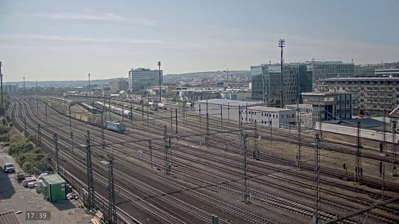 A wide shot of numerous train tracks extending into the distance under a clear sky, with buildings and parked trains visible in the background.