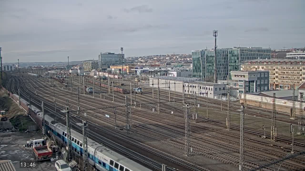 A nighttime view of a train yard with several tracks and buildings in the background, possibly under light snow or rain.
