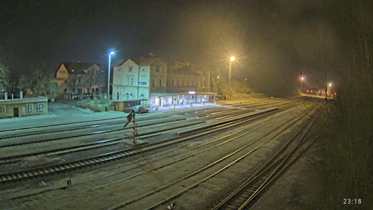 A nighttime view of a train station with several tracks extending into the distance under hazy, dimly lit conditions.