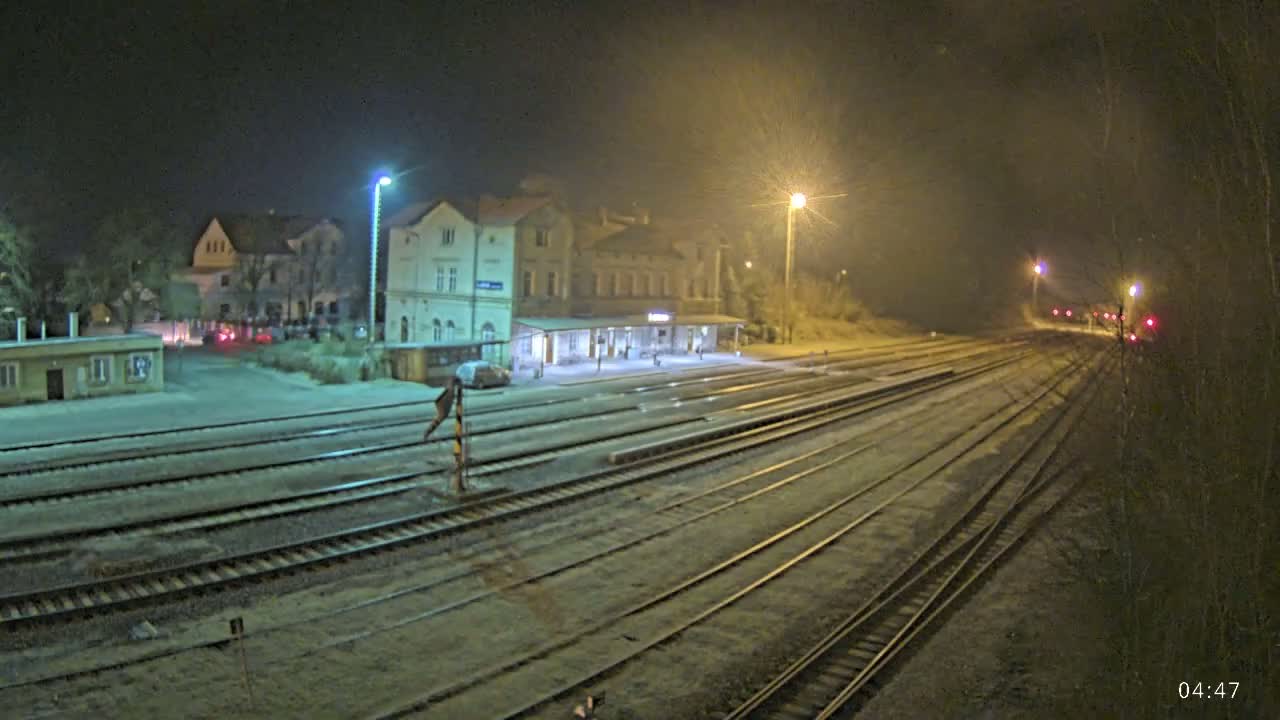 A nighttime view of a train station with multiple tracks extending into the distance under hazy, dimly lit conditions.