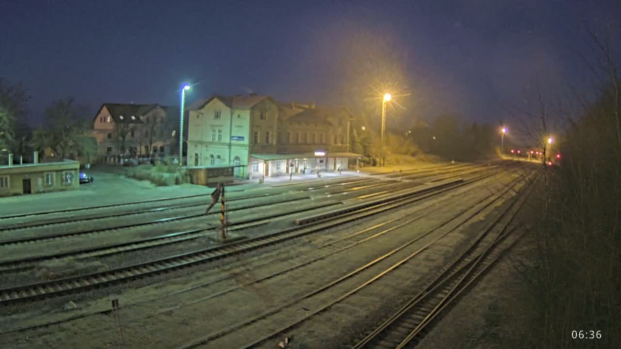 A nighttime view of a train station with multiple train tracks extending into the distance under a dark, possibly cloudy sky.