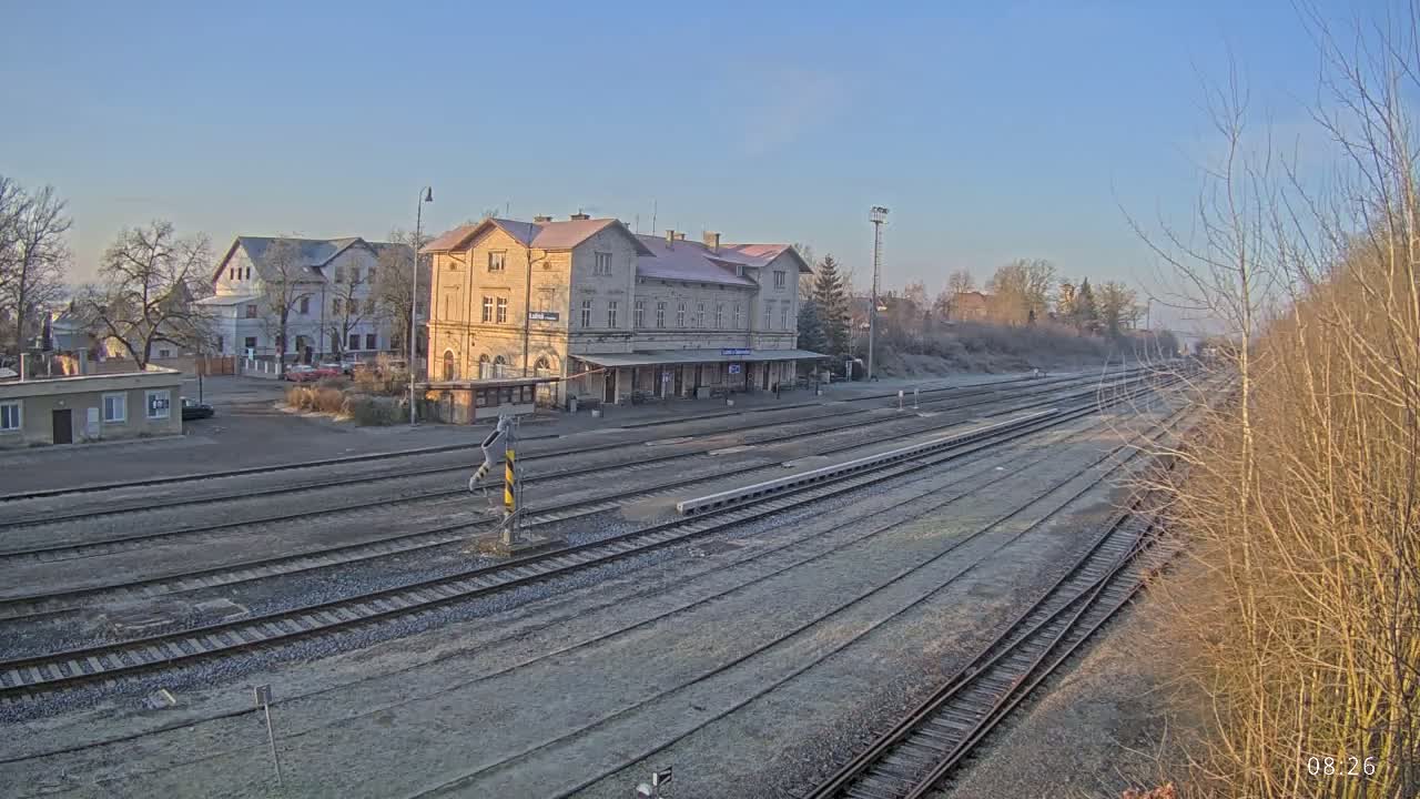 A train station with a large building and multiple train tracks stretches into the distance on a clear, frosty morning.