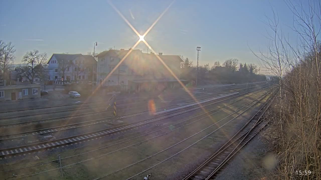 A train station with several tracks is seen bathed in the bright sunlight of a clear day.