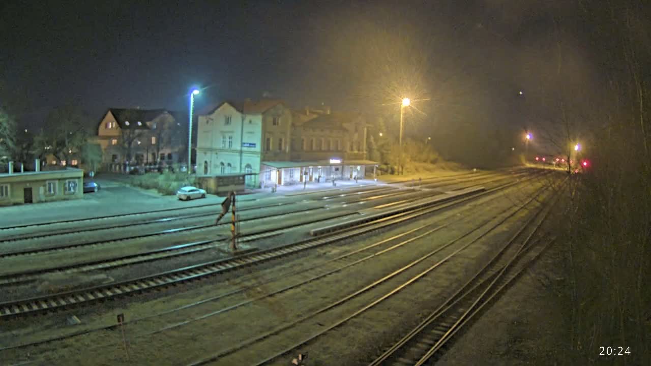 A nighttime view of a train station with multiple tracks extending into the distance under hazy or foggy conditions.