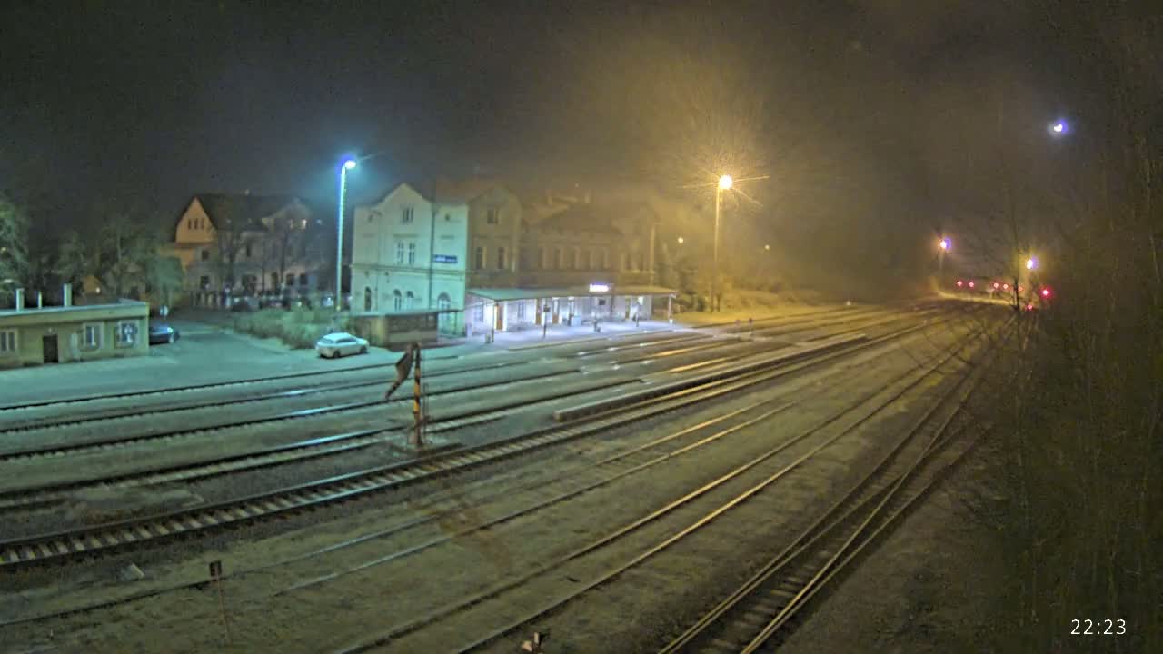 A nighttime view of a train station with multiple tracks extending into the distance under hazy or foggy conditions.