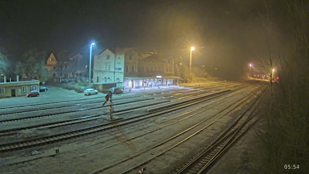 A nighttime view of a snow-covered train station with several tracks extending into the distance under hazy, dimly lit conditions.