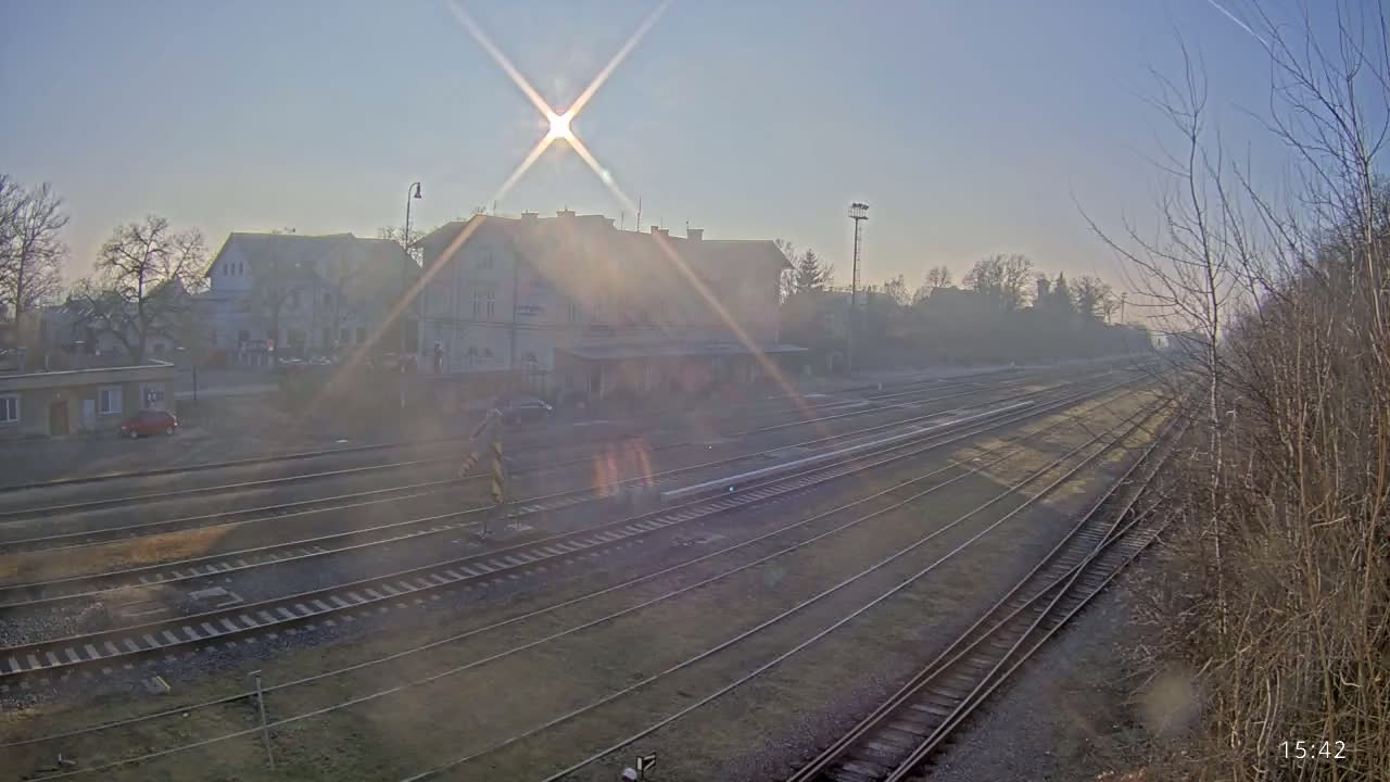 A train station with multiple tracks is shown on a hazy, sunny day.