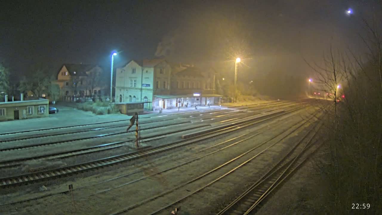 A train station at night in foggy conditions, with multiple sets of tracks extending into the distance.