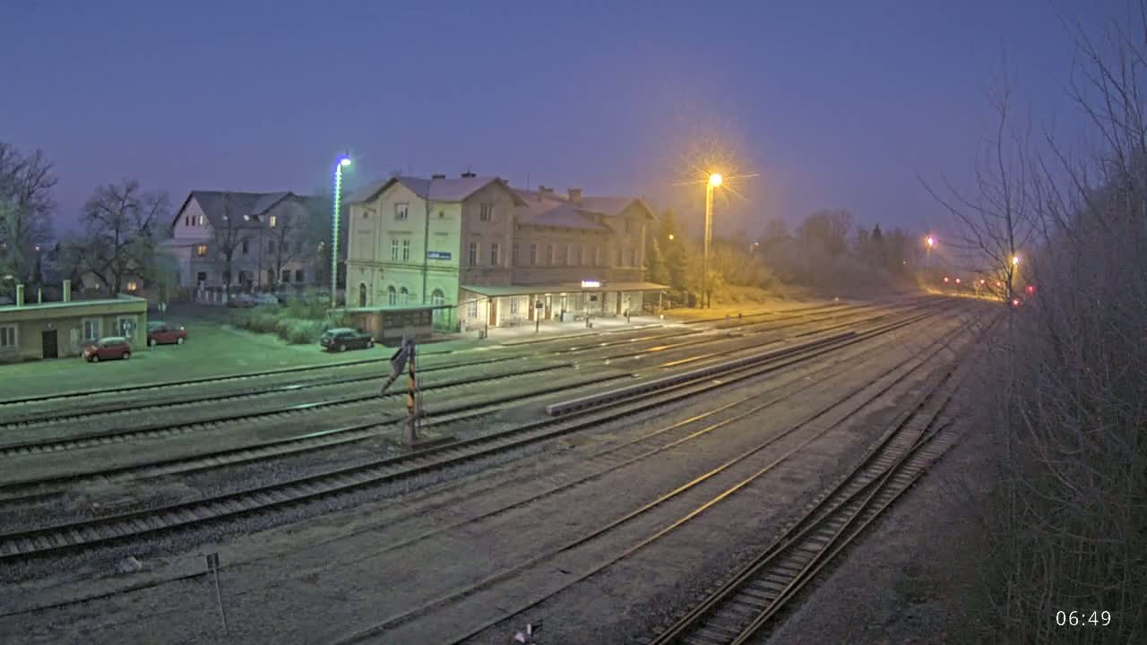 A train station with a long expanse of train tracks under a twilight sky, possibly with light frost on the ground.