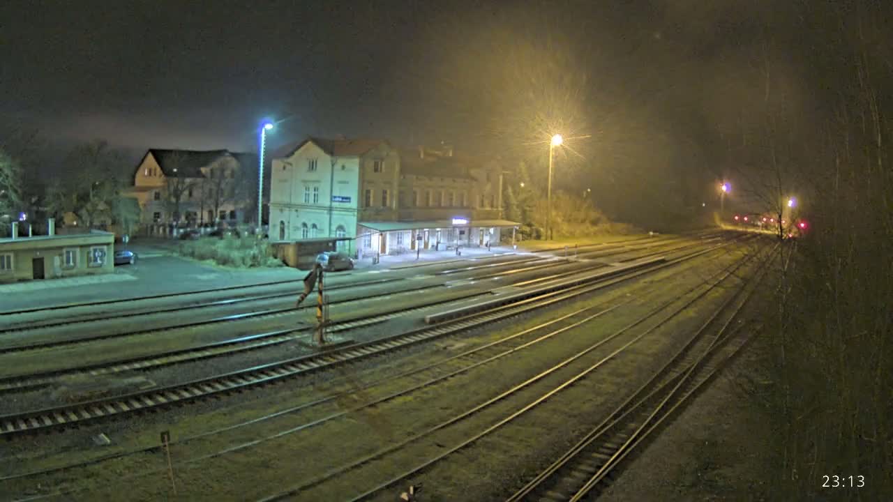 A nighttime view of a train station with multiple tracks extending into the distance under hazy, dimly lit conditions.