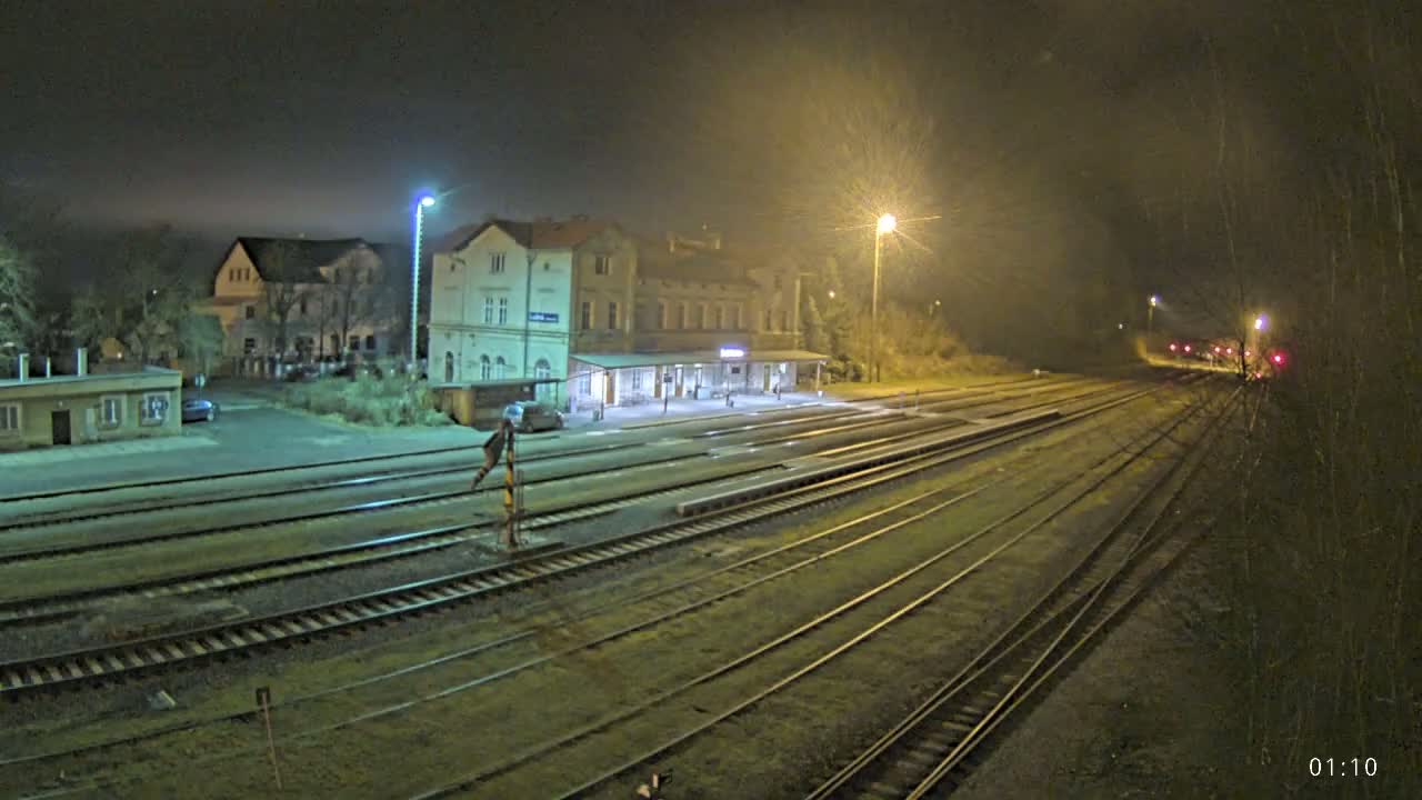 A nighttime view of a train station with several tracks extending into the distance under a foggy sky illuminated by streetlights.