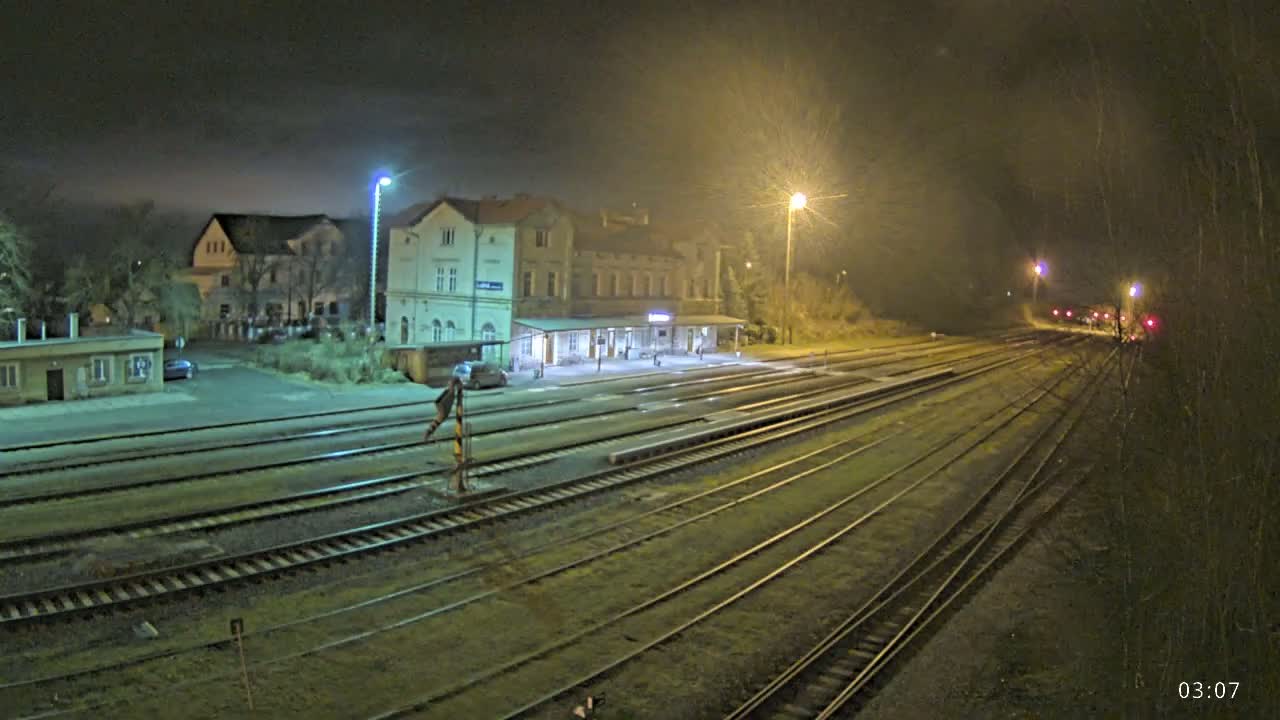 A nighttime view of a train station with several tracks extending into the distance under hazy, dimly lit conditions.