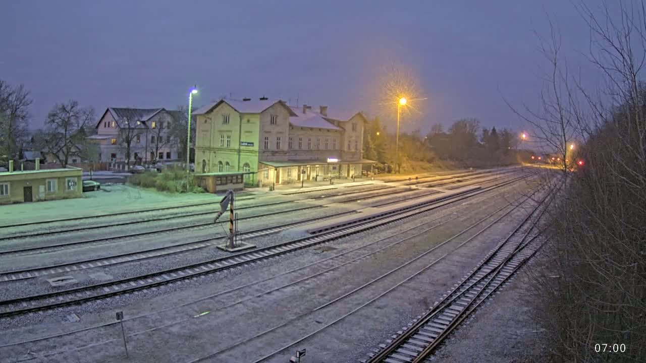 A snow-covered train station with multiple tracks extending into the distance under a twilight sky.
