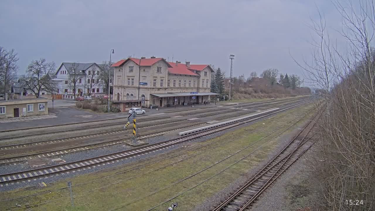 A train station with a long platform and multiple tracks, situated under an overcast sky.