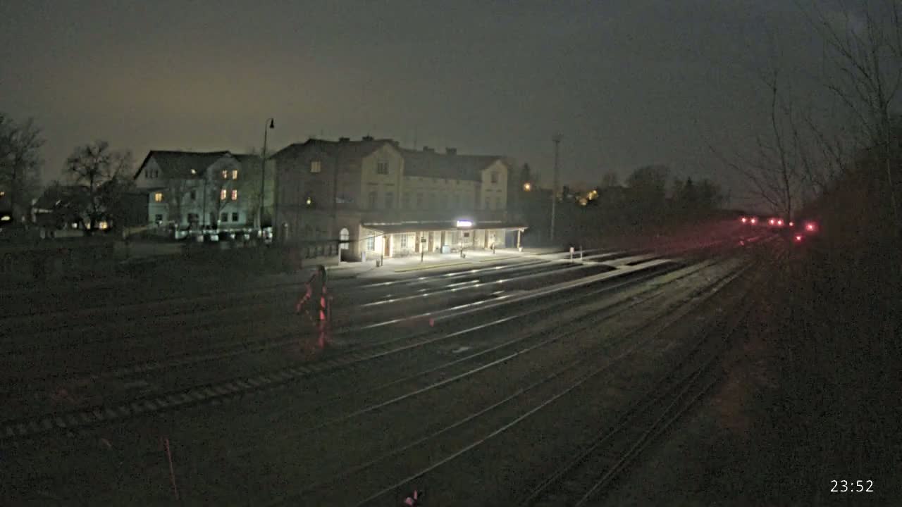 A nighttime view of a dimly lit train station with multiple tracks extending into the distance under a dark, overcast sky.