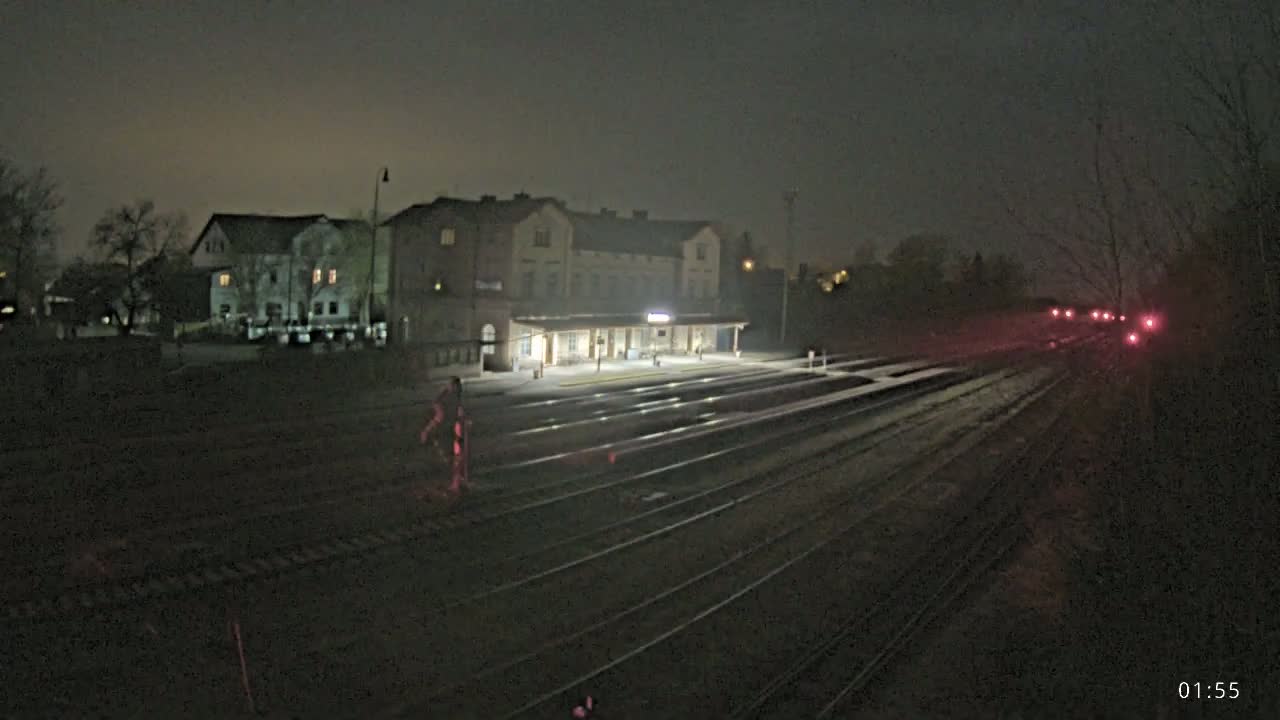 A nighttime view of a train station with multiple tracks extending into the distance under a dark, possibly foggy sky.