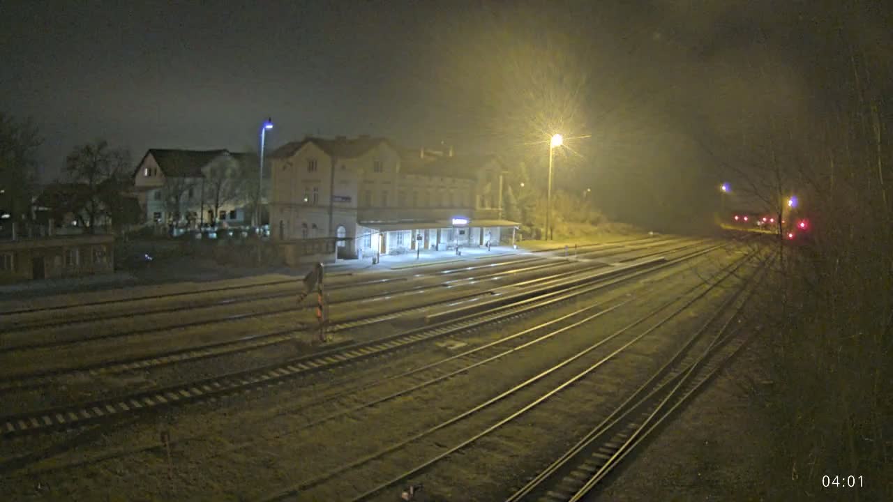 A nighttime view of a train station with multiple tracks extending into the distance under hazy conditions.