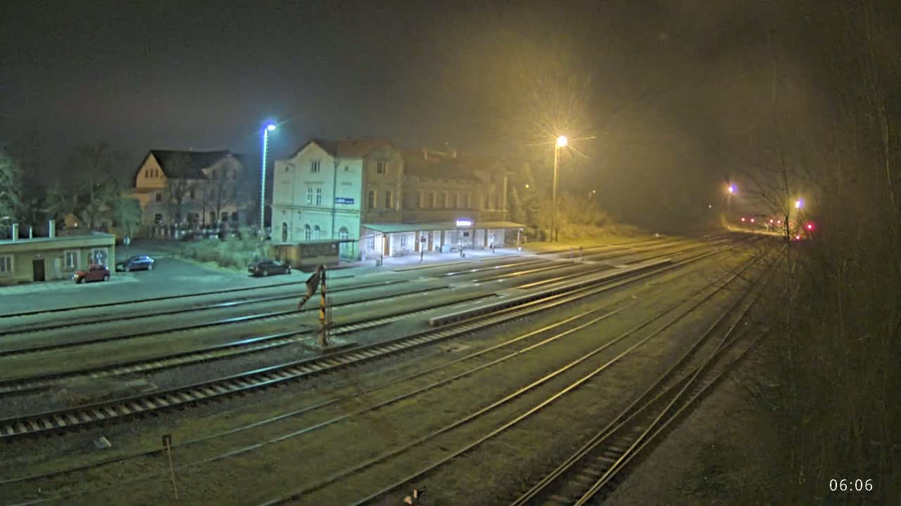 A train station at night in foggy conditions, with several sets of train tracks extending into the distance.