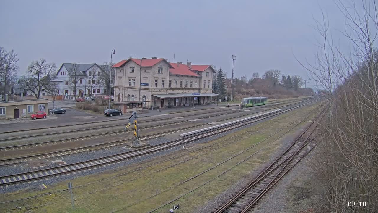 A train station with a long platform and several train tracks is visible on an overcast day.
