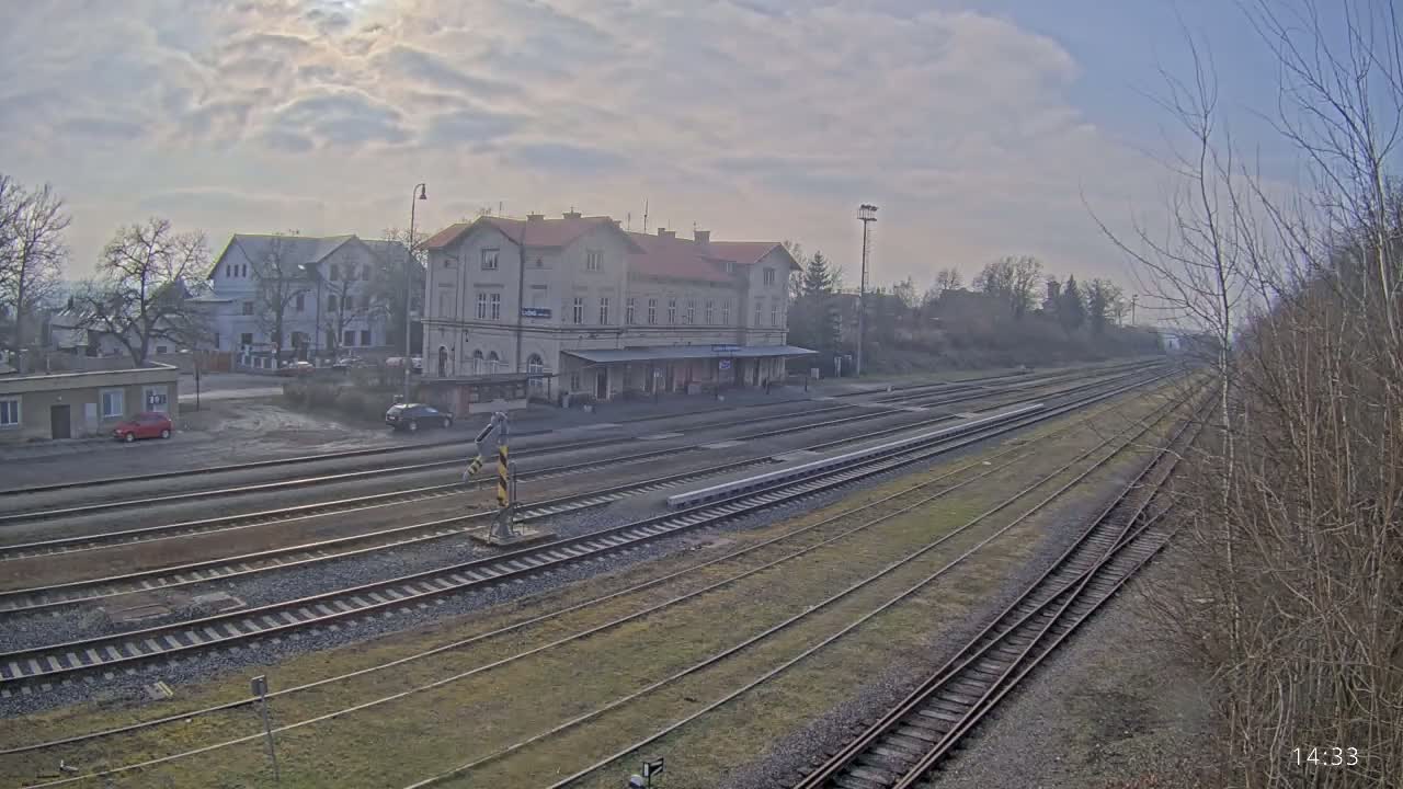 A train station with a long platform and multiple train tracks stretches into the distance under a cloudy sky.