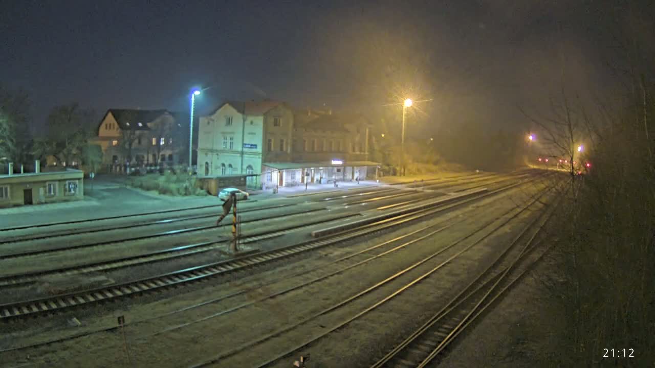 A nighttime view of a train station with multiple tracks extending into the hazy distance, illuminated by streetlights.