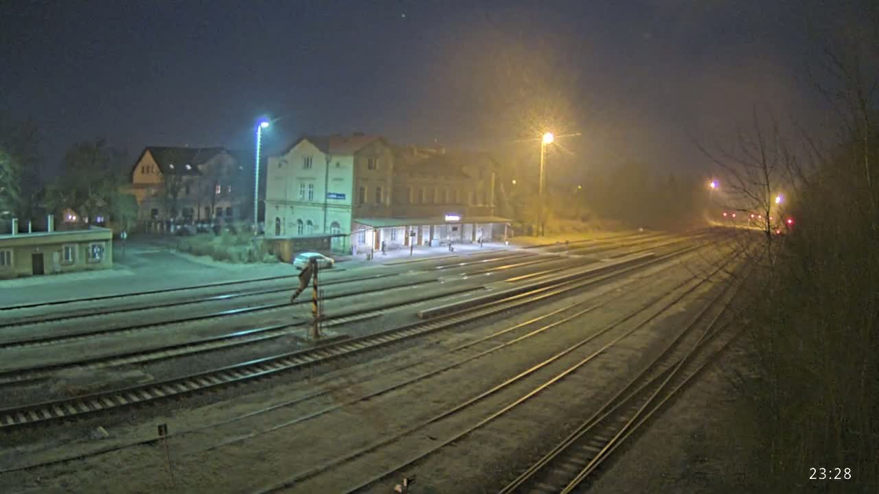 A nighttime view of a train station with several tracks extending into the foggy distance, illuminated by streetlights.