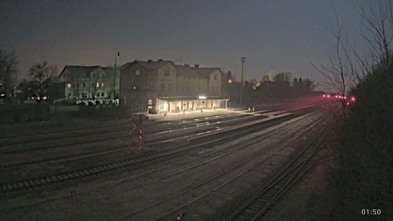 A dimly lit train station at night, under a dark sky, with several sets of train tracks extending into the distance.