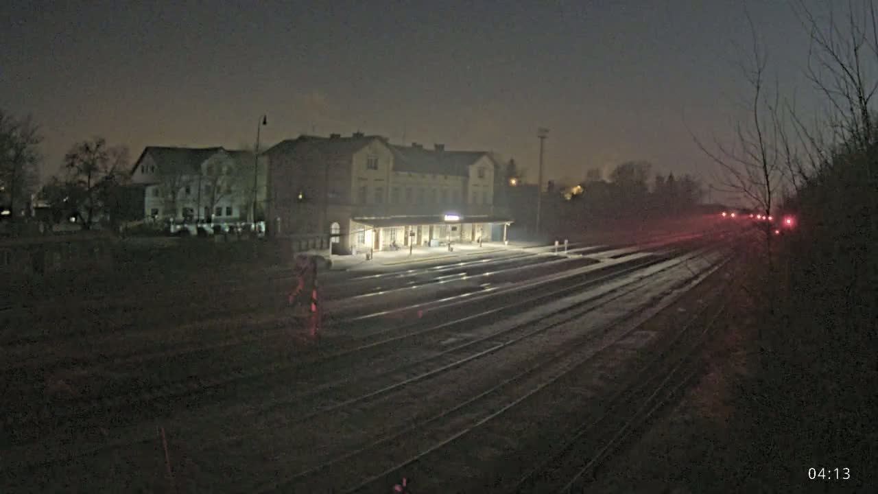 A dimly lit train station at night, with several sets of train tracks extending into the distance under a dark, possibly foggy sky.