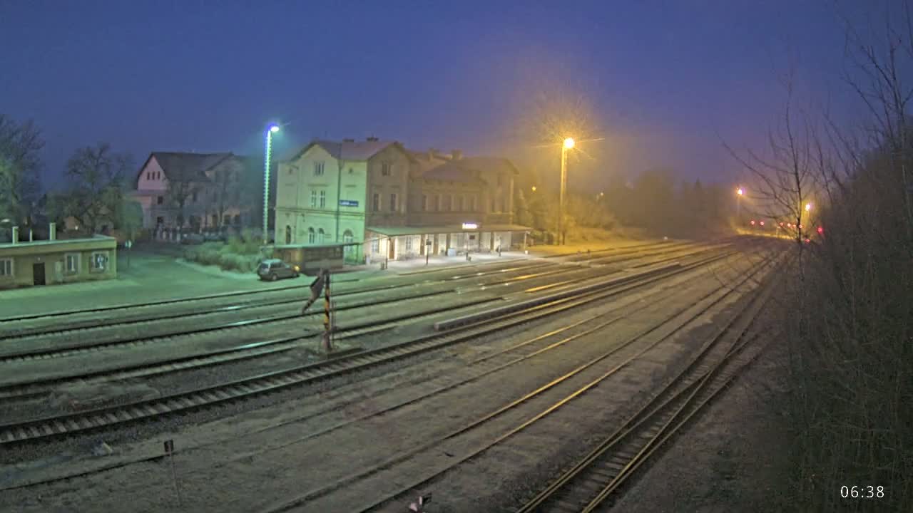 A train station at night in foggy conditions, with several train tracks extending into the distance.