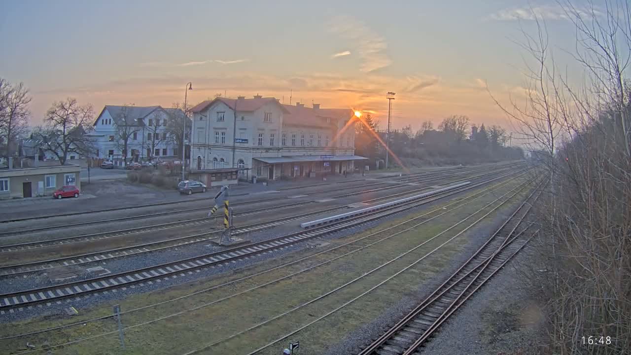 A train station with a large building sits beside several train tracks at sunset.