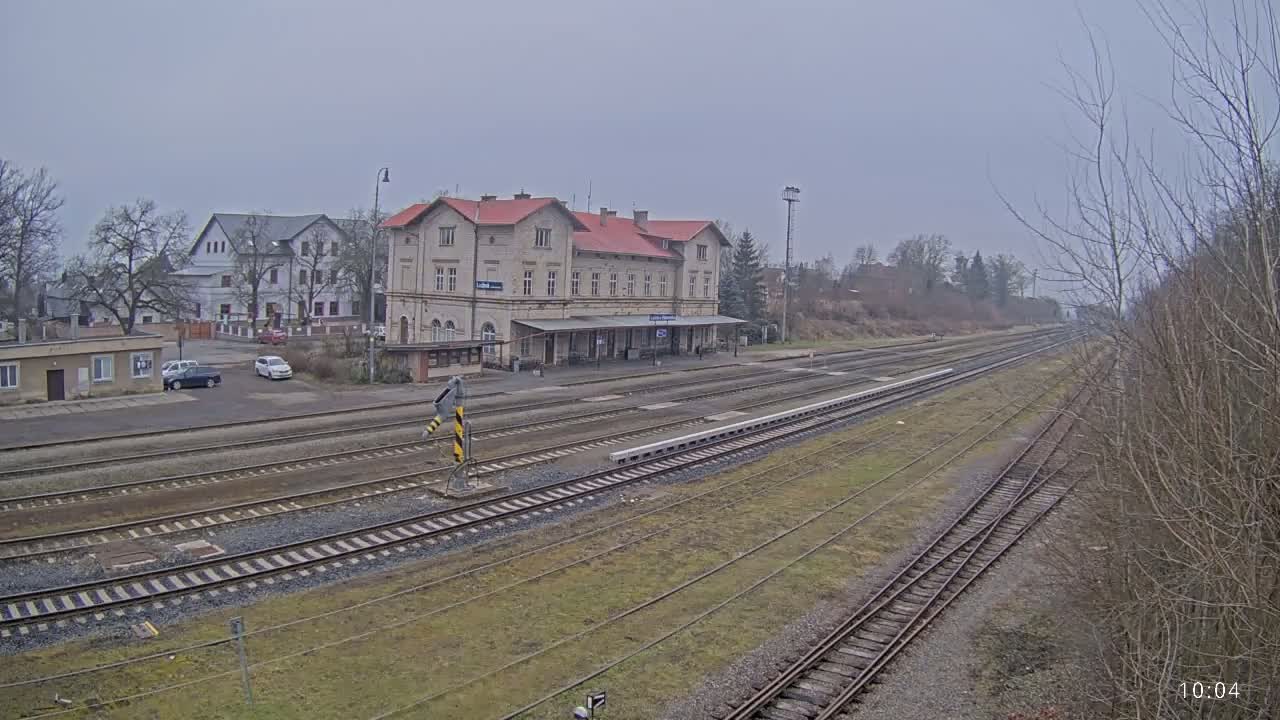 A long view of a train station with a large building and multiple train tracks on an overcast day.