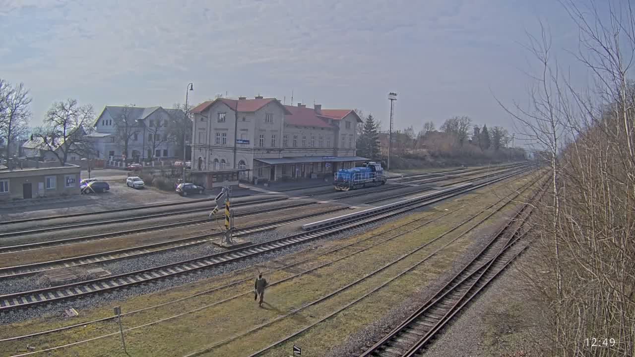 A blue locomotive sits at a train station with multiple tracks on a partly cloudy day.