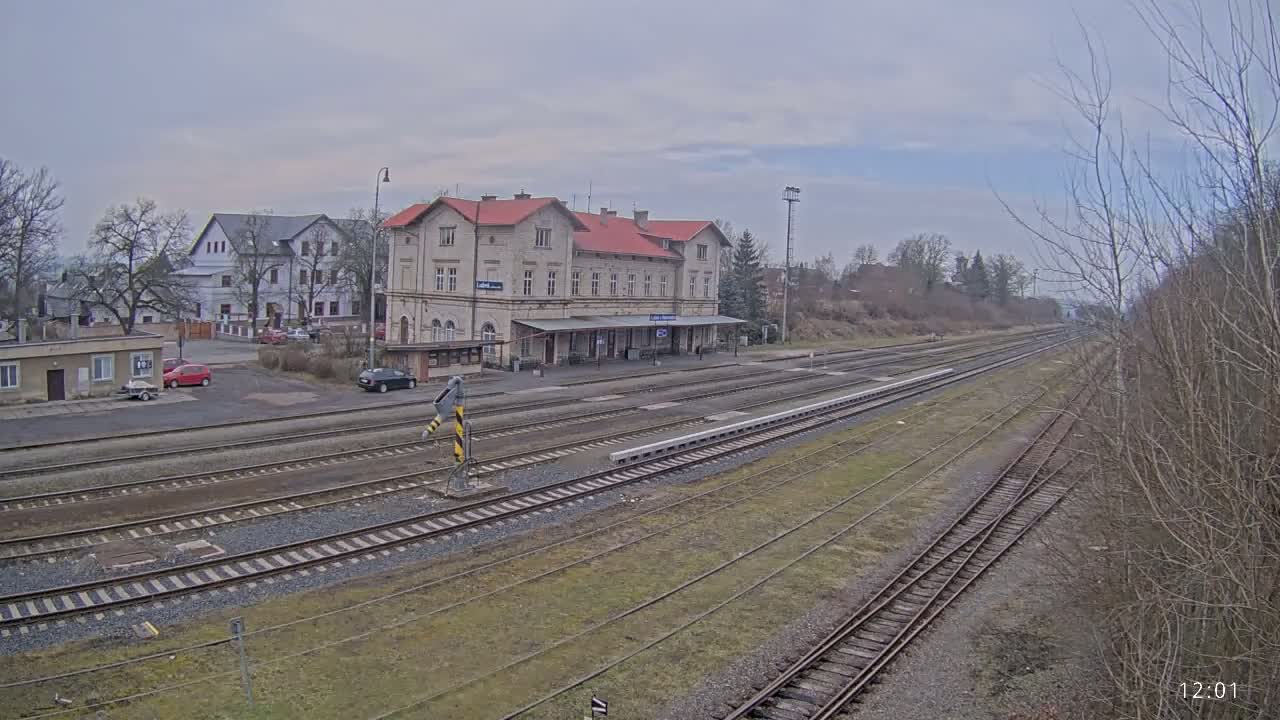 A long view of a train station with a light-colored building and multiple train tracks under an overcast sky.