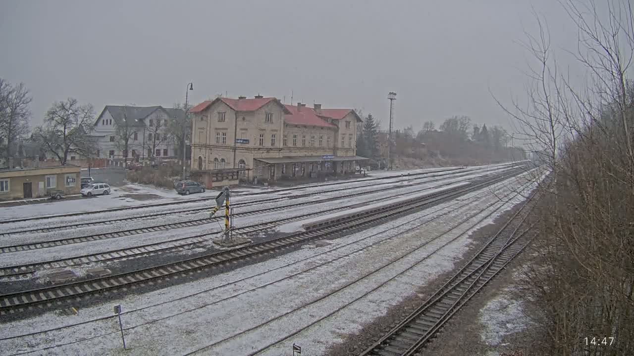 A snow-covered train station with multiple tracks extends into the distance under an overcast sky.