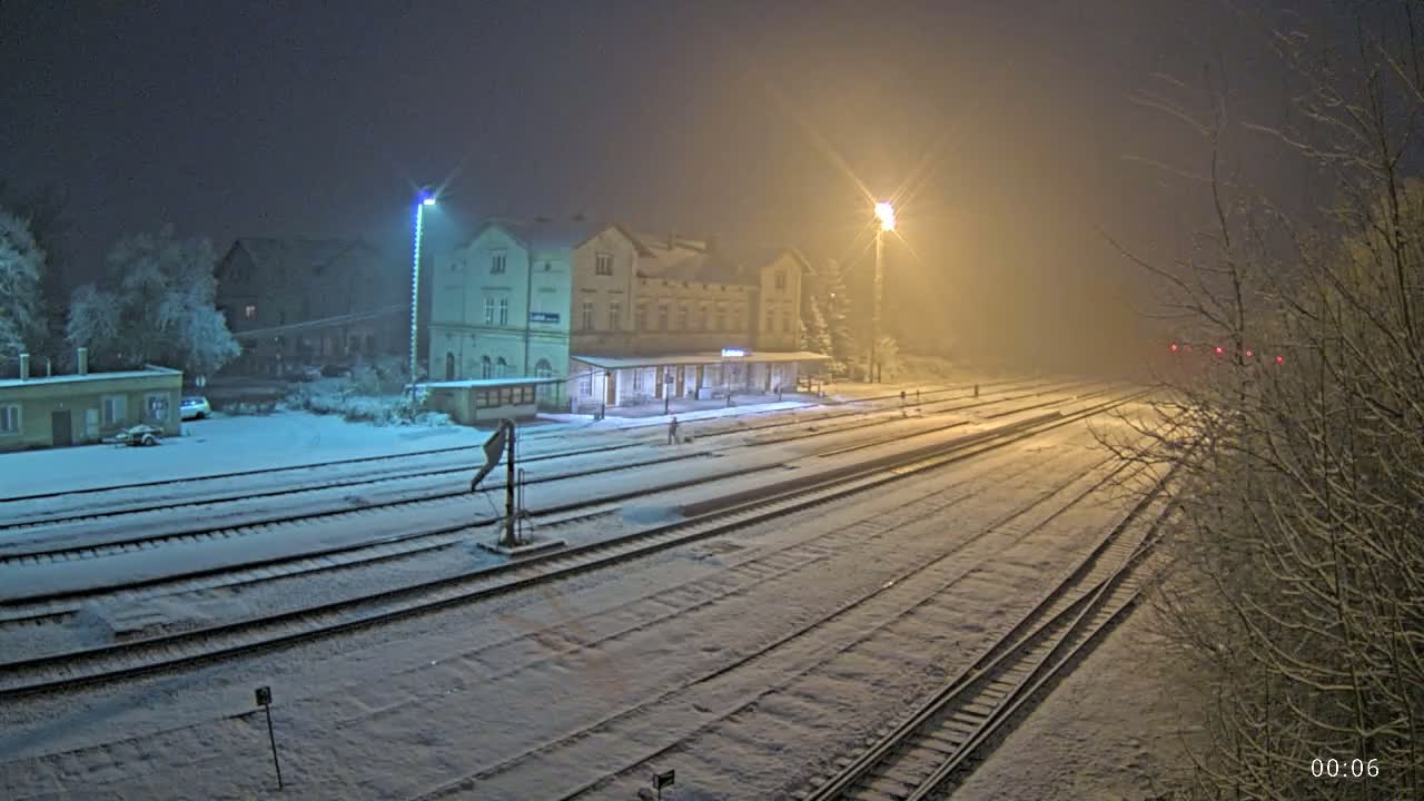 A snow-covered train station at night, illuminated by streetlights, with several tracks extending into the foggy distance.