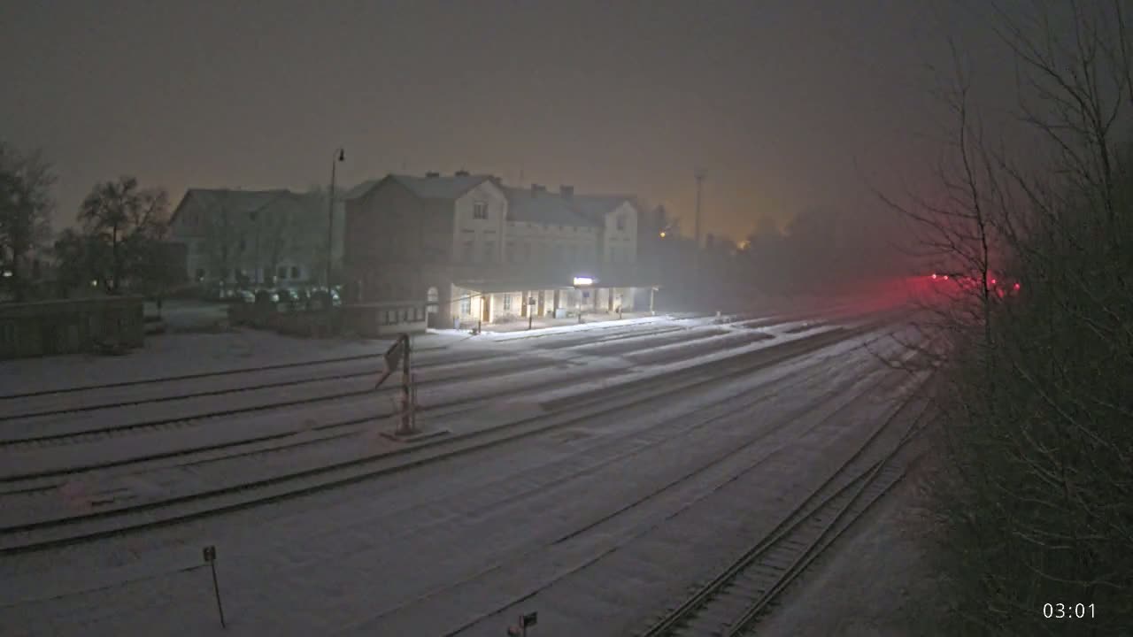 A snow-covered train station and tracks are visible under a hazy, nighttime sky.