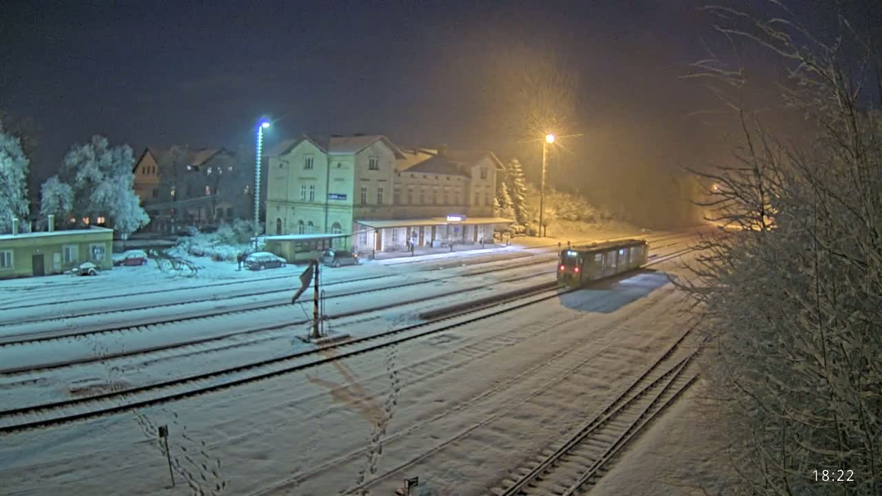 A train sits at a snow-covered train station at night under hazy, dimly lit conditions.