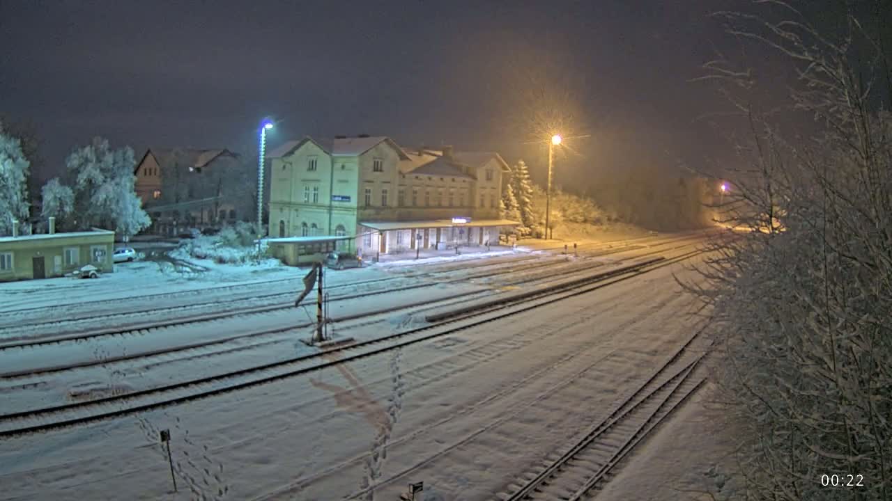 A snow-covered train station at night, illuminated by streetlights, with train tracks extending into the distance.