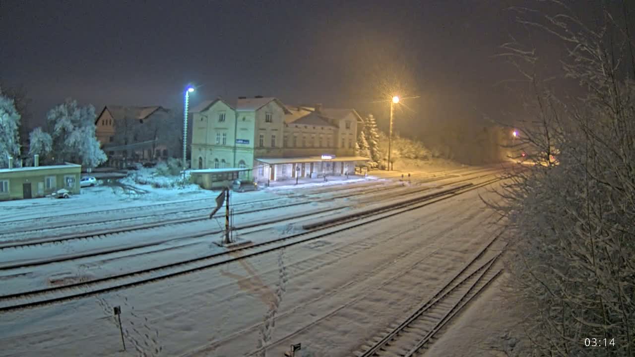 A snow-covered train station at night, illuminated by streetlights, with tracks extending into the distance.