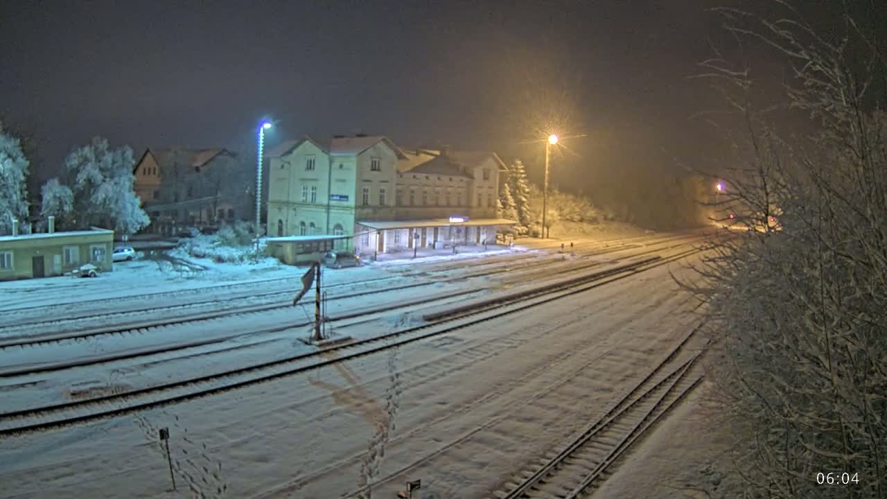 A snow-covered train station and tracks are illuminated at night by streetlights.