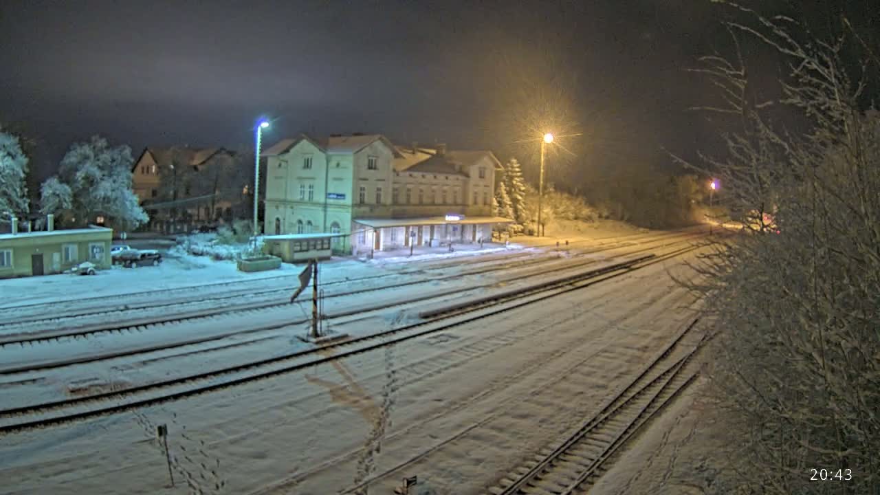 A snow-covered train station and tracks are illuminated at night by streetlights.