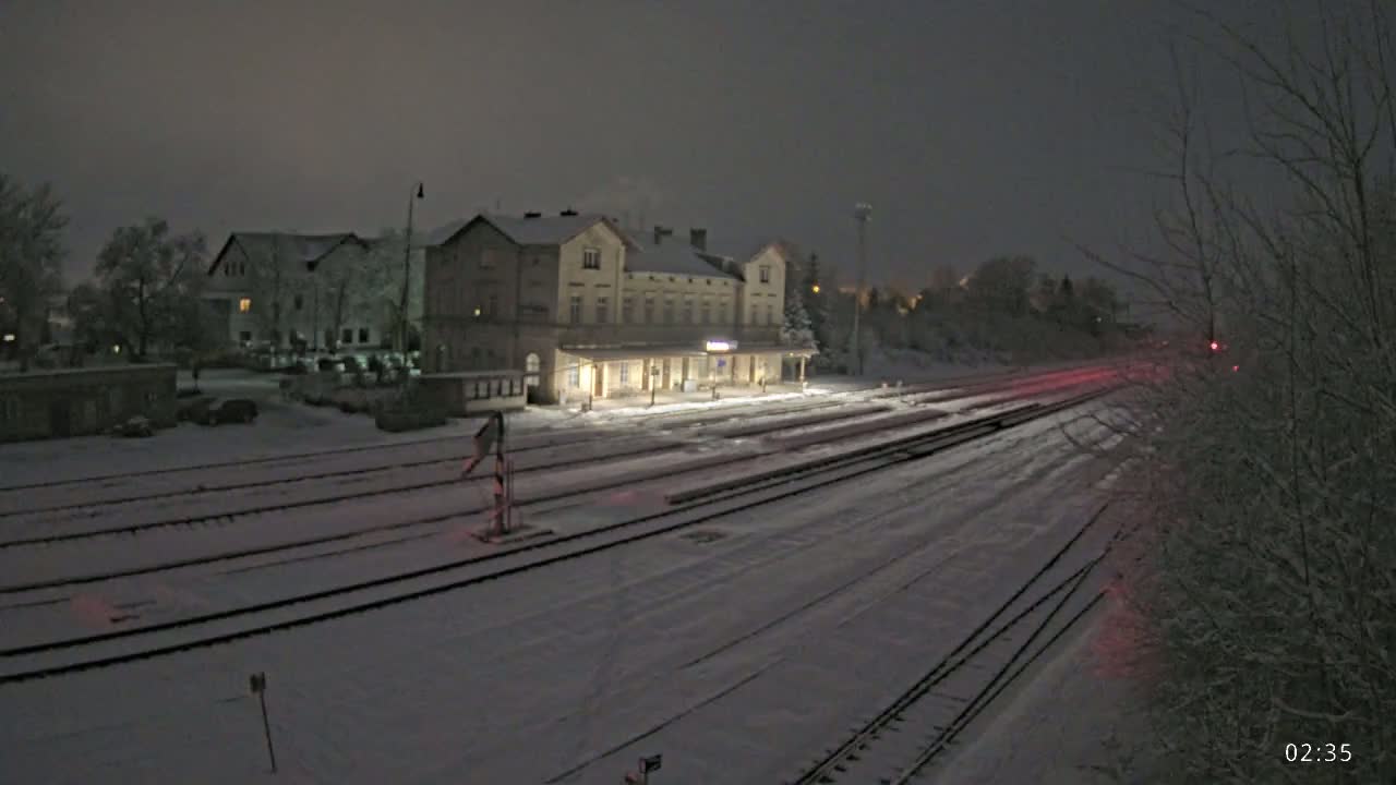 A snow-covered train station and tracks are illuminated at night.