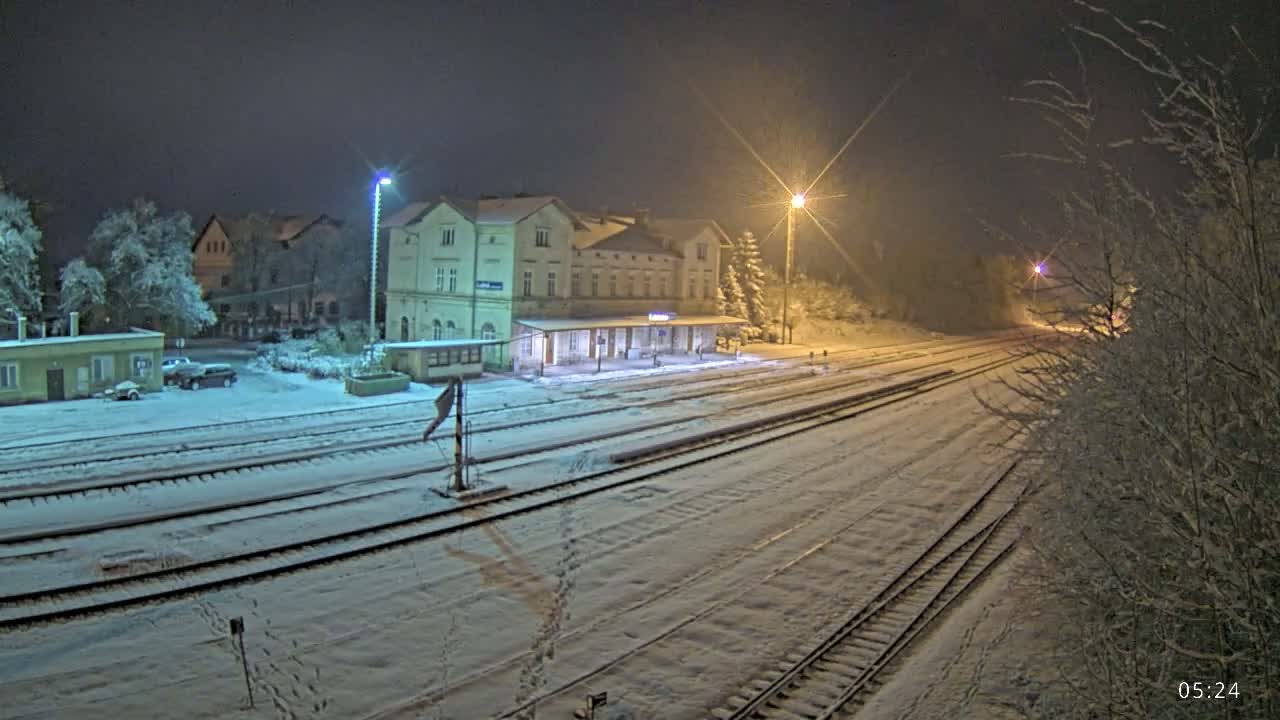 A snow-covered train station at night, illuminated by streetlights, with a long expanse of tracks leading away from the station.