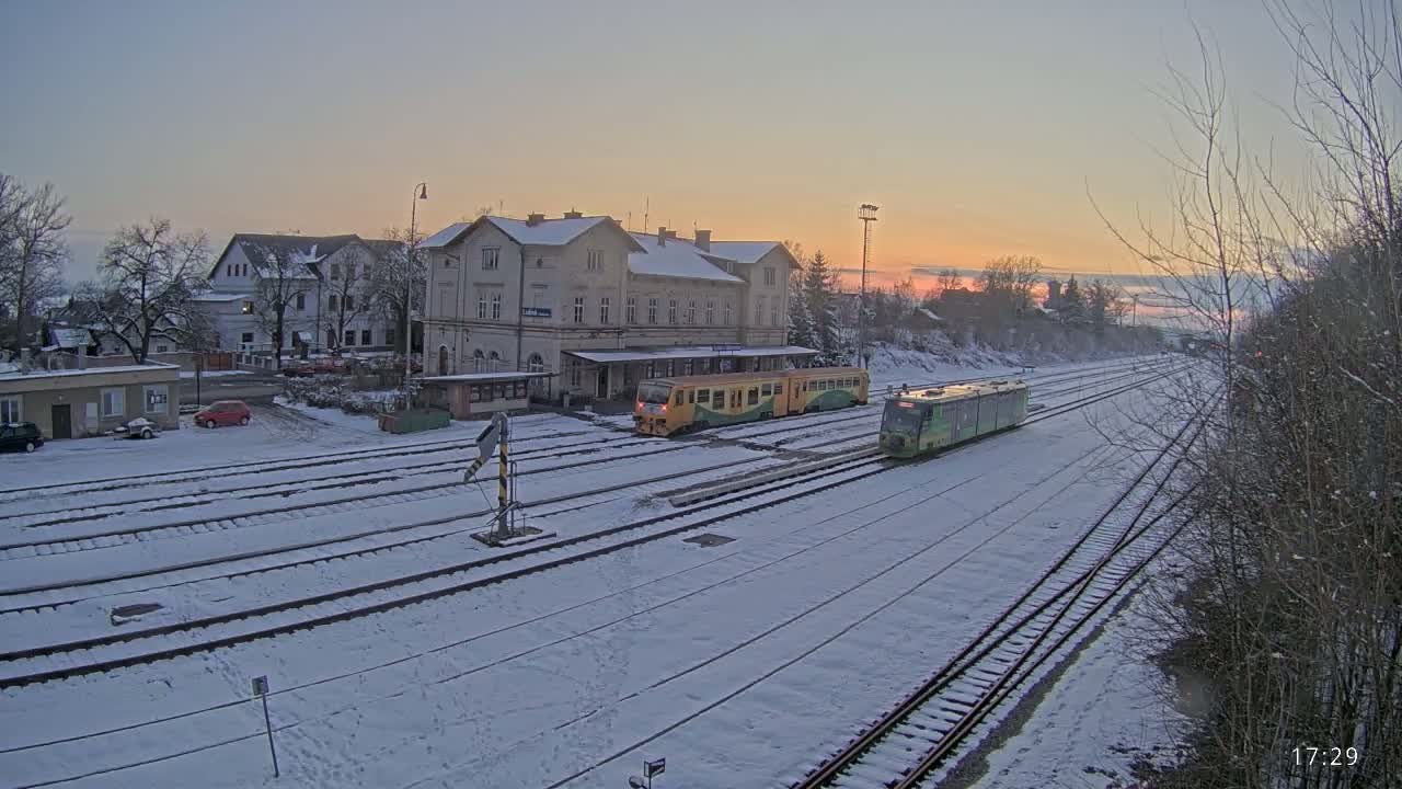 Two trains are at a snow-covered train station during a sunset.